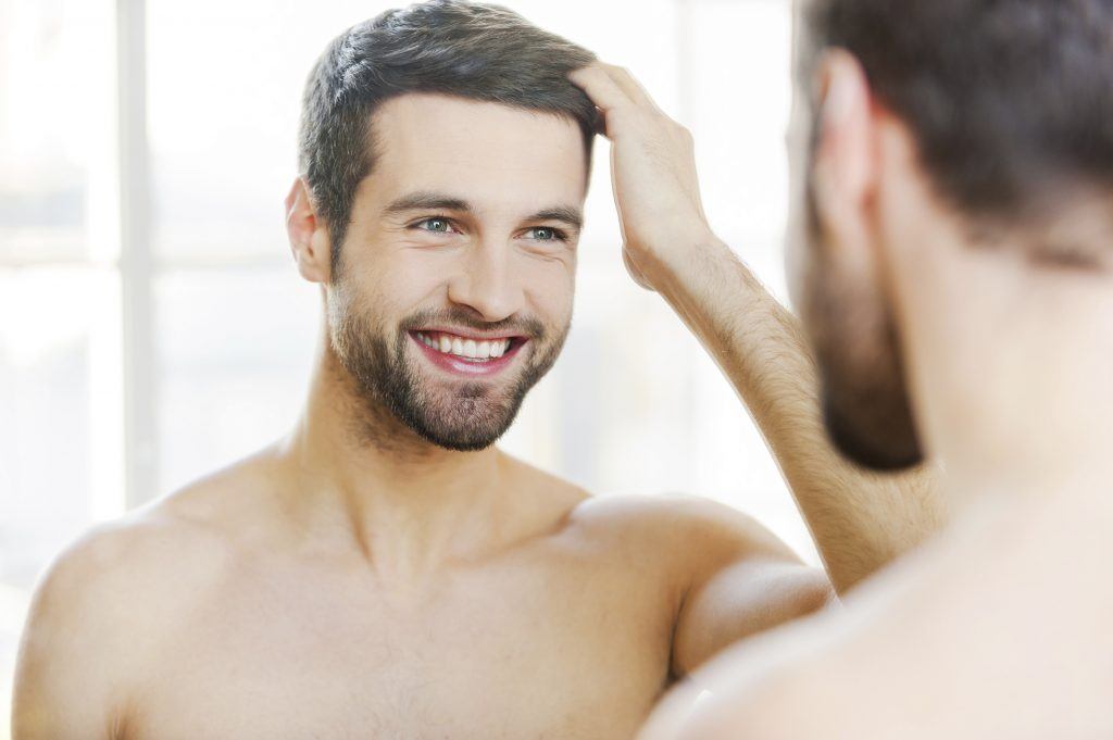 Man smiling and touching hair in the mirror