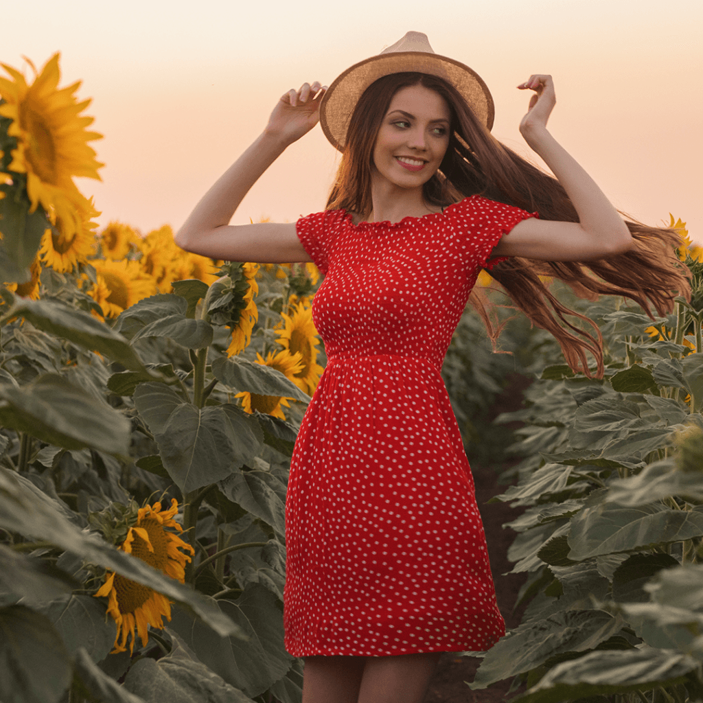 Woman in red dress and straw hat standing in sunflower field