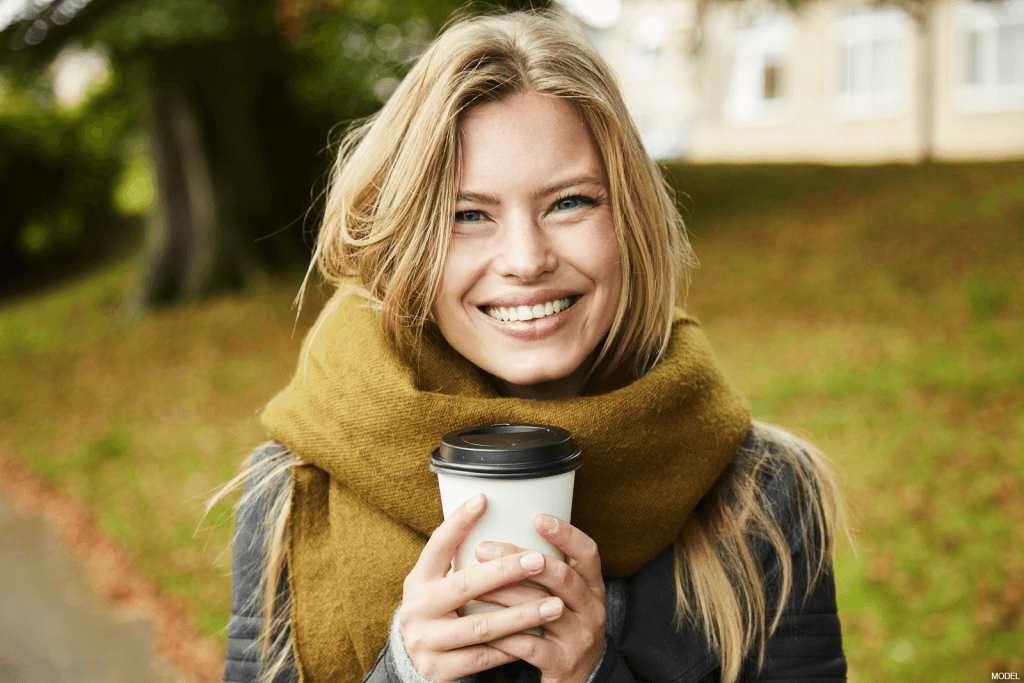 Woman smiling while wearing a large scarf and holding a coffee cup