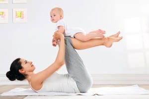 Woman lies on ground and holds baby in the air