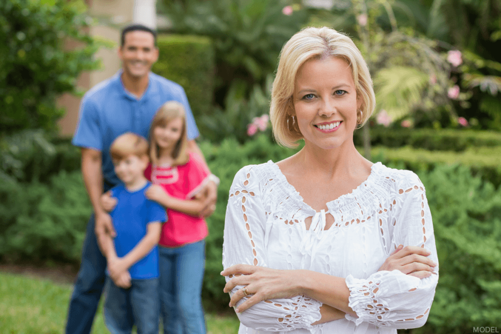 Woman smiling outdoors with man, boy child, and girl child smiling in the background