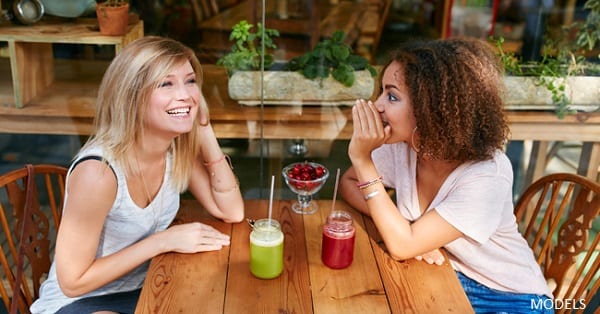 Two women talking happily together at an outdoor table while sipping on smoothies
