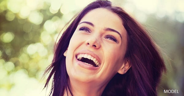 A young brunette woman smiling against a backdrop of green leaves