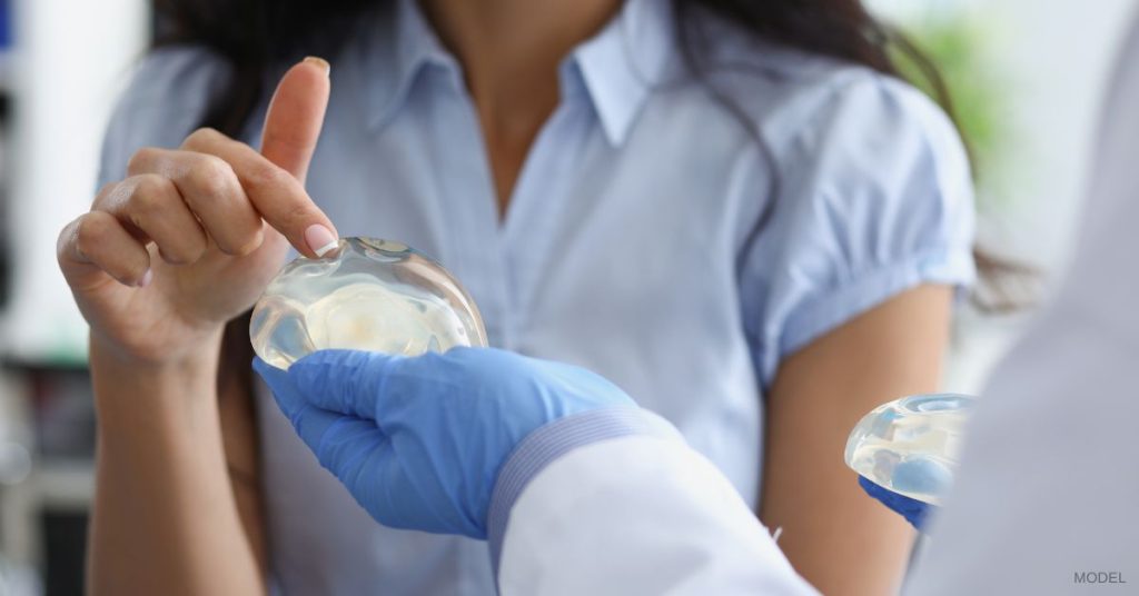 Woman (model) standing in a plastic surgeon's office, feeling different types of breast implants.