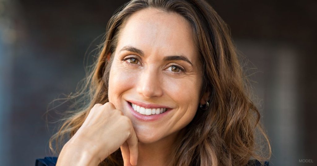 Woman (MODEL) smiling while resting her head on her hand.